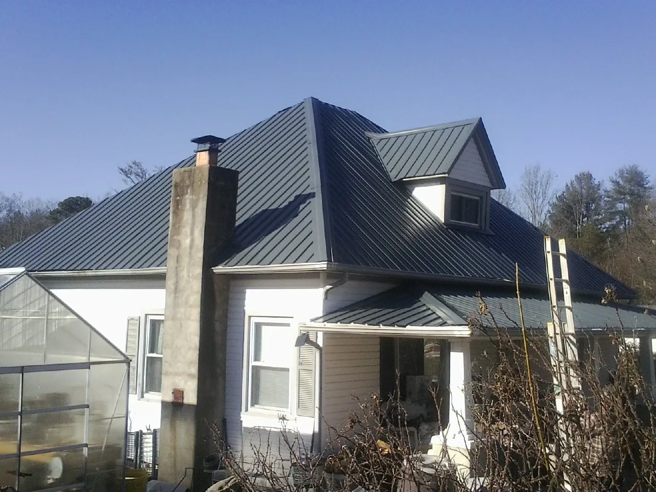 Dark blue standing seam metal roof on a white farmhouse with dormer — Slate & Tile Roof Repair by Roofing Brothers in Cerritos