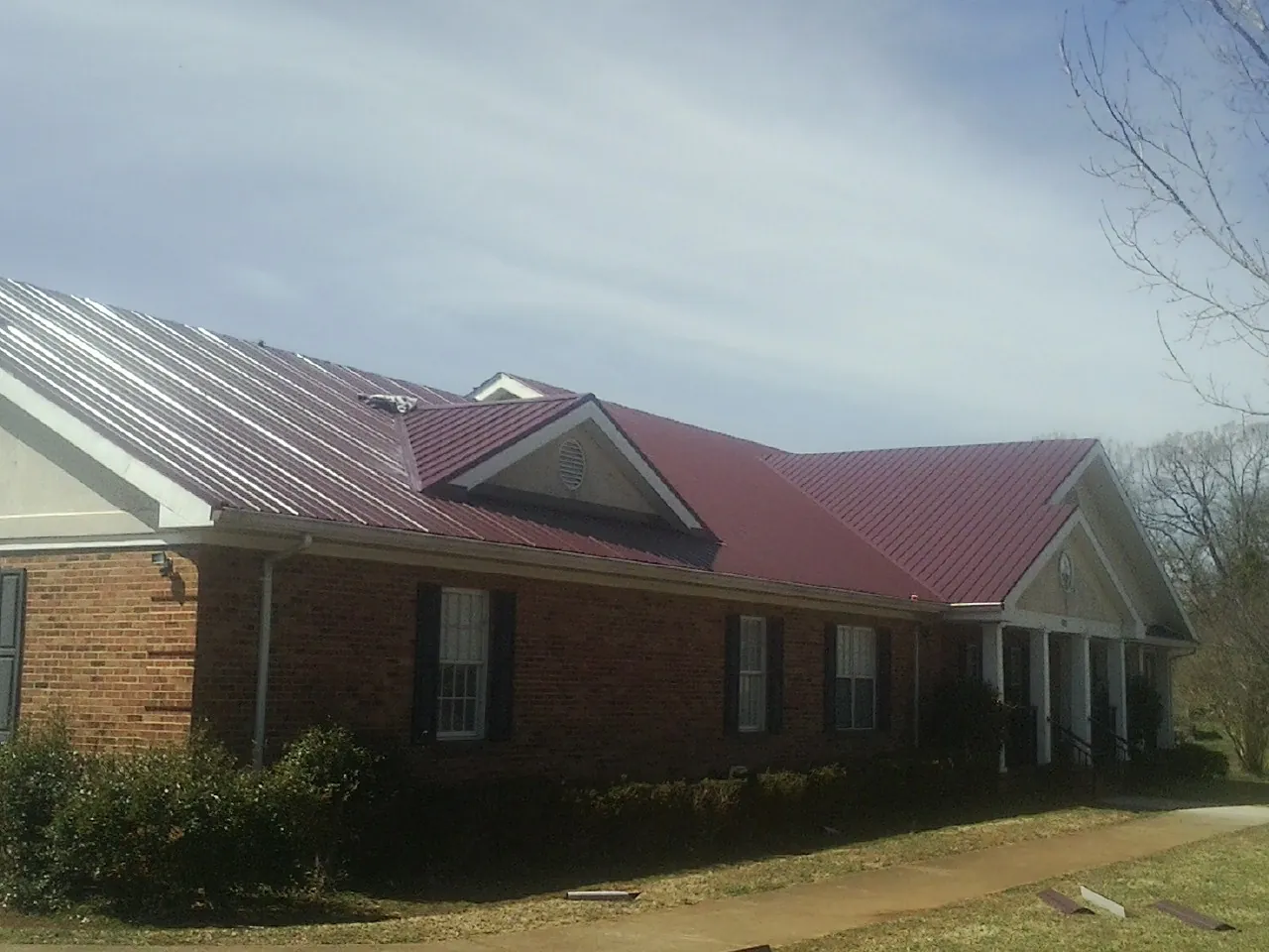 Red metal roof with gabled entries on a long brick building, from a Hail Damage Roof Repair job in Cerritos