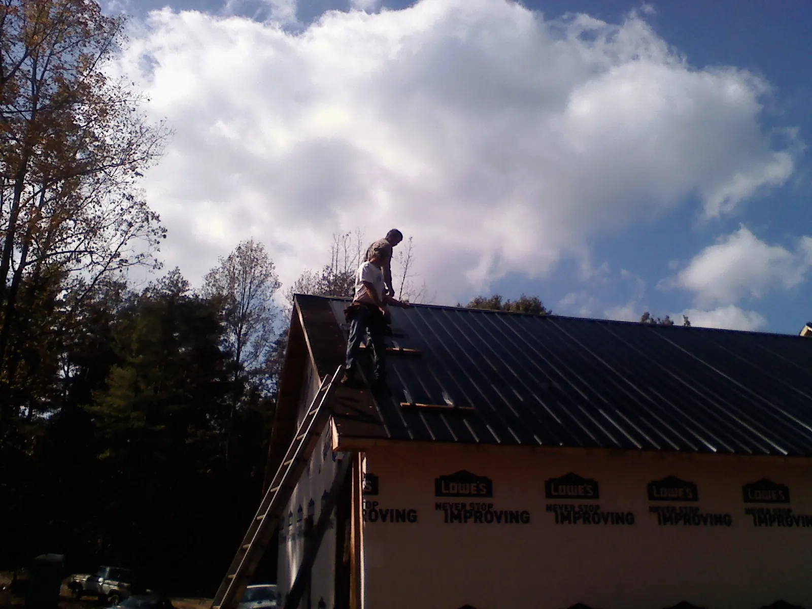 Roofer fastening dark metal panels high against a cloudy sky, from a Roof Inspection job in Cerritos