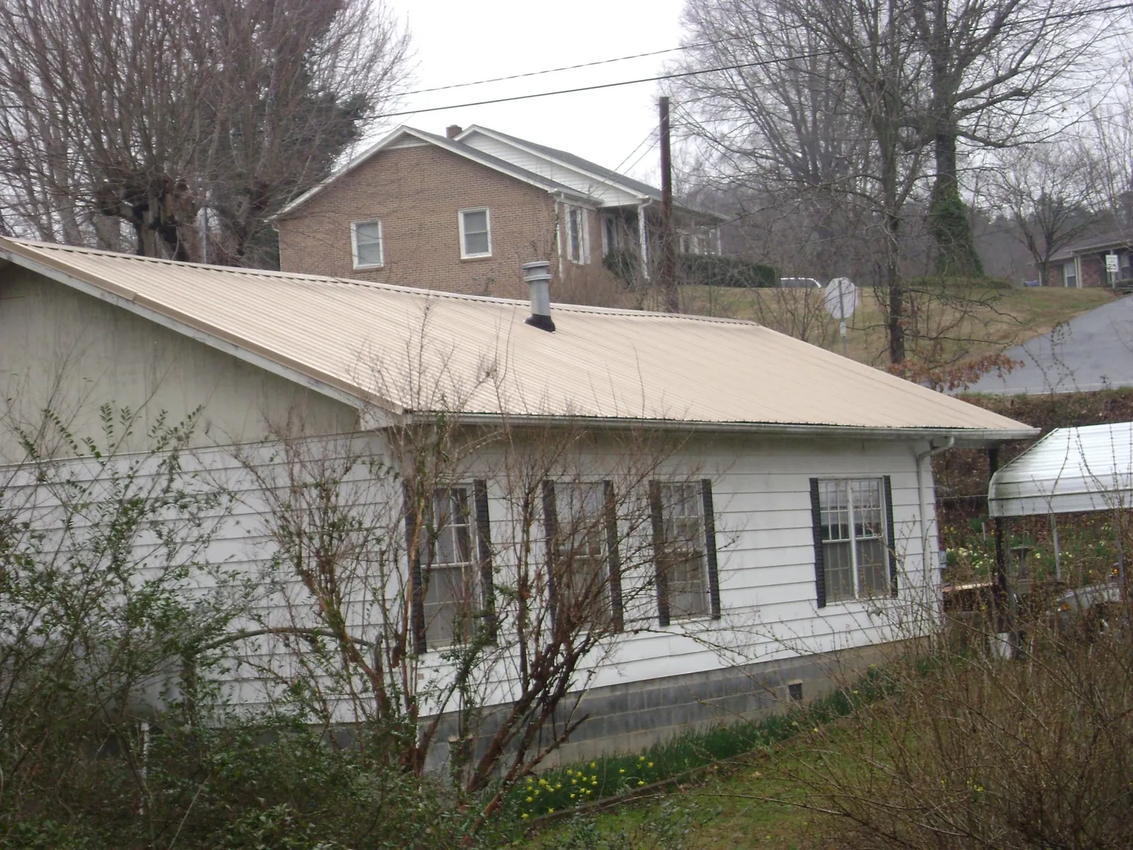 Tan metal roof on a white sided house set into a hillside — Commercial Roofing by Roofing Brothers in Cerritos